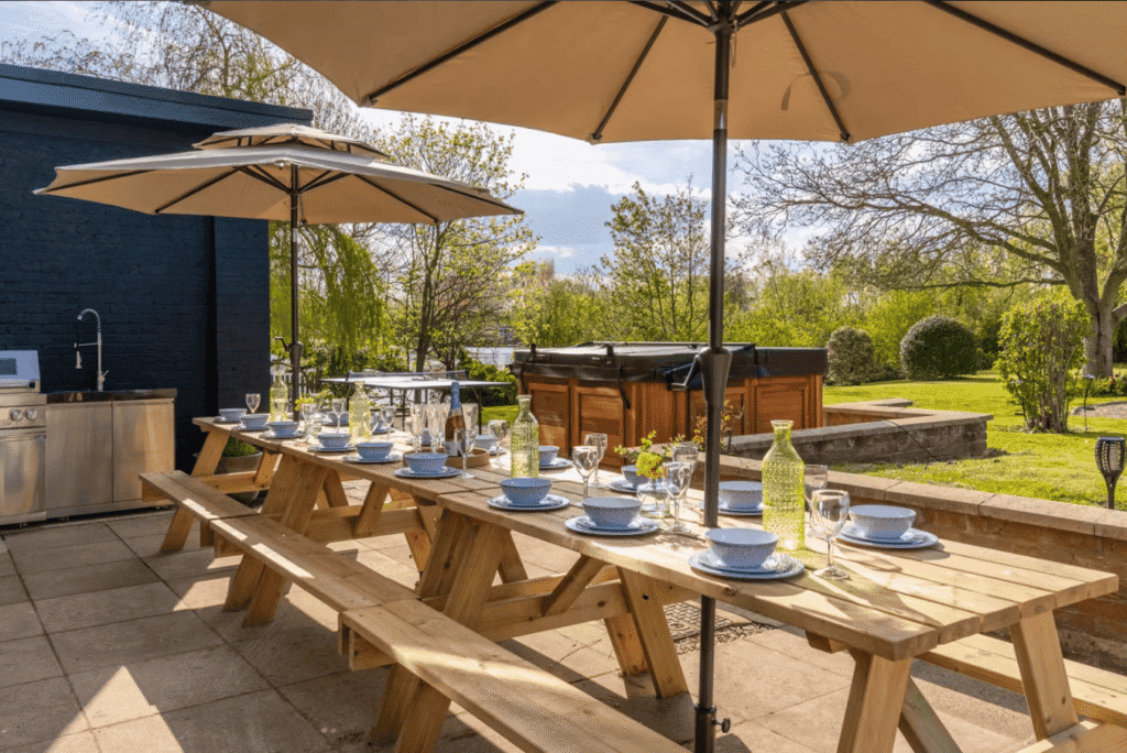 A luxury hen party house garden featuring a private hot tub, modern outdoor kitchen, and a beautifully laid dining table for a large group celebration.